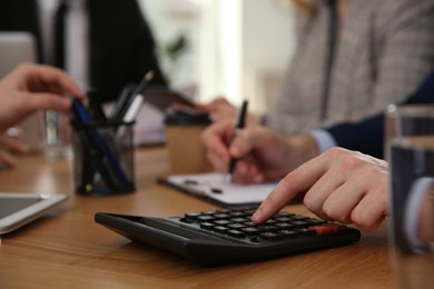 Photo of Man using calculator at table in office during business meeting, closeup. Management consulting