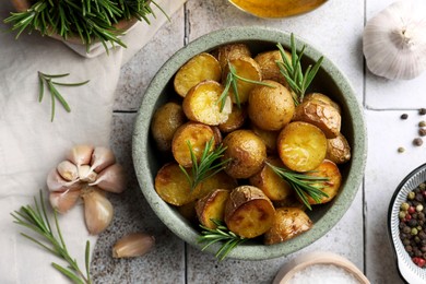 Flat lay composition with tasty baked potato and aromatic rosemary on light tiled table