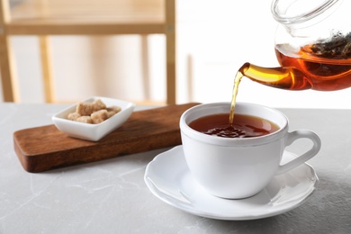 Pouring black tea into white porcelain cup on gray table