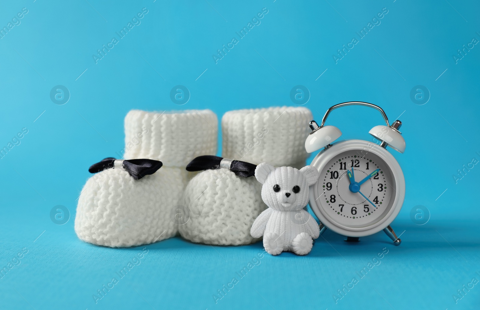 Photo of Alarm clock, toy bear and baby booties on light blue background. Time to give birth