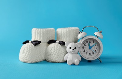 Alarm clock, toy bear and baby booties on light blue background. Time to give birth
