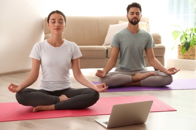 Photo of Couple practicing yoga while watching online class at home during coronavirus pandemic. Social distancing