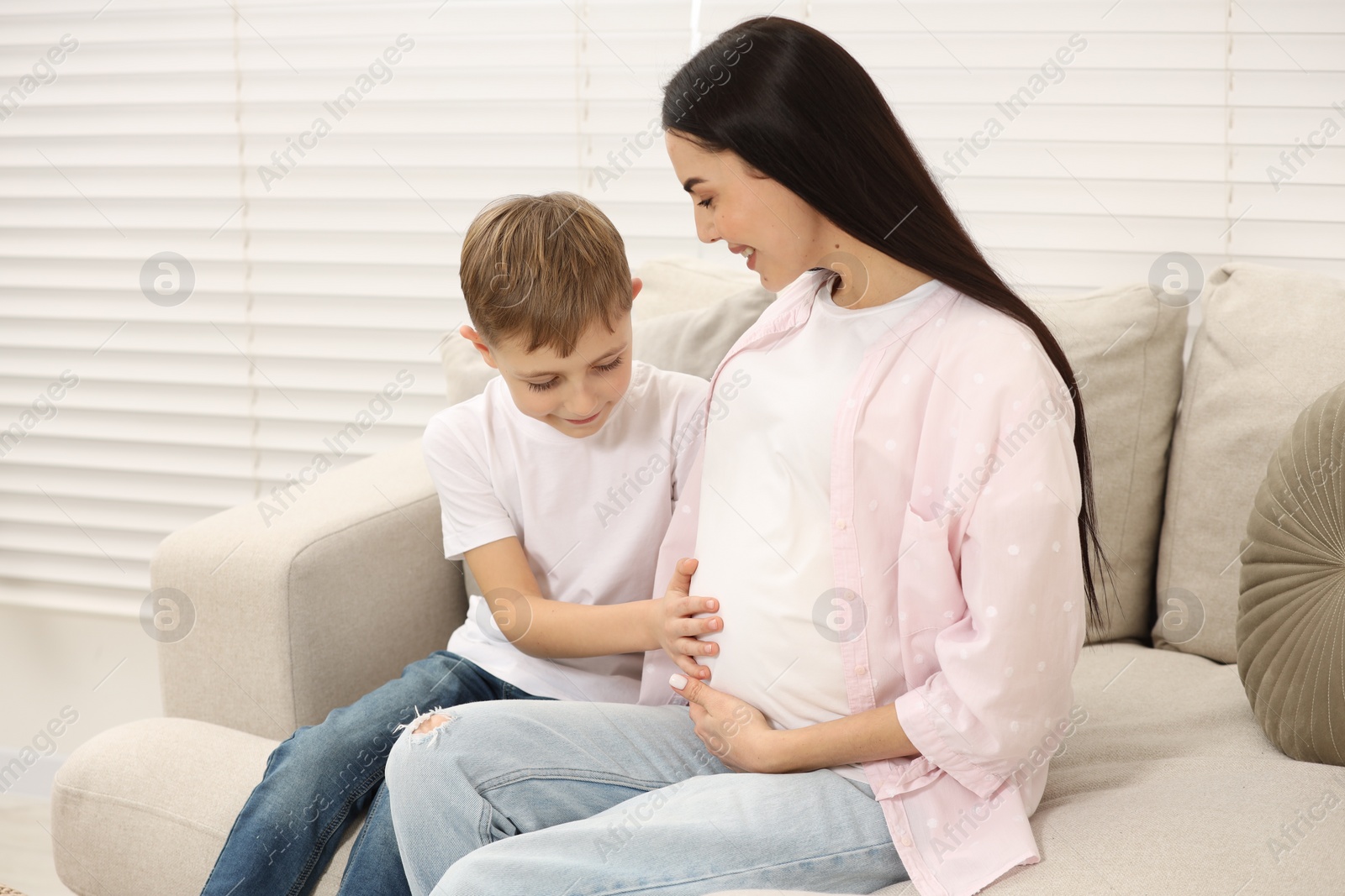 Photo of Cute boy touching pregnant mother's belly at home