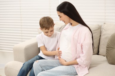 Cute boy touching pregnant mother's belly at home