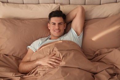 Photo of Man lying in bed with brown linens at home, above view
