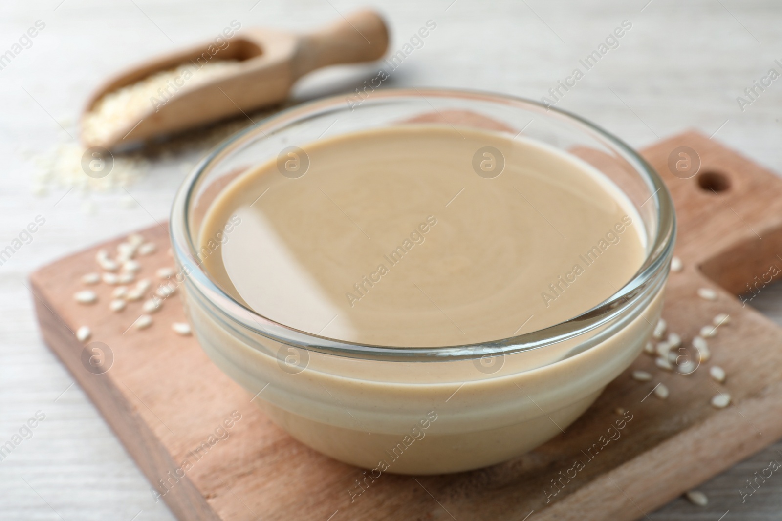 Photo of Tasty sesame paste in glass bowl on wooden board, closeup