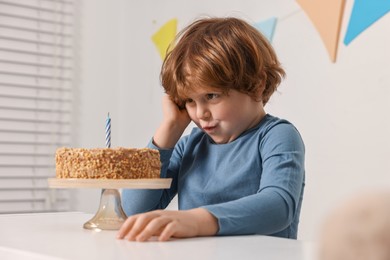 Cute boy with birthday cake at white table indoors