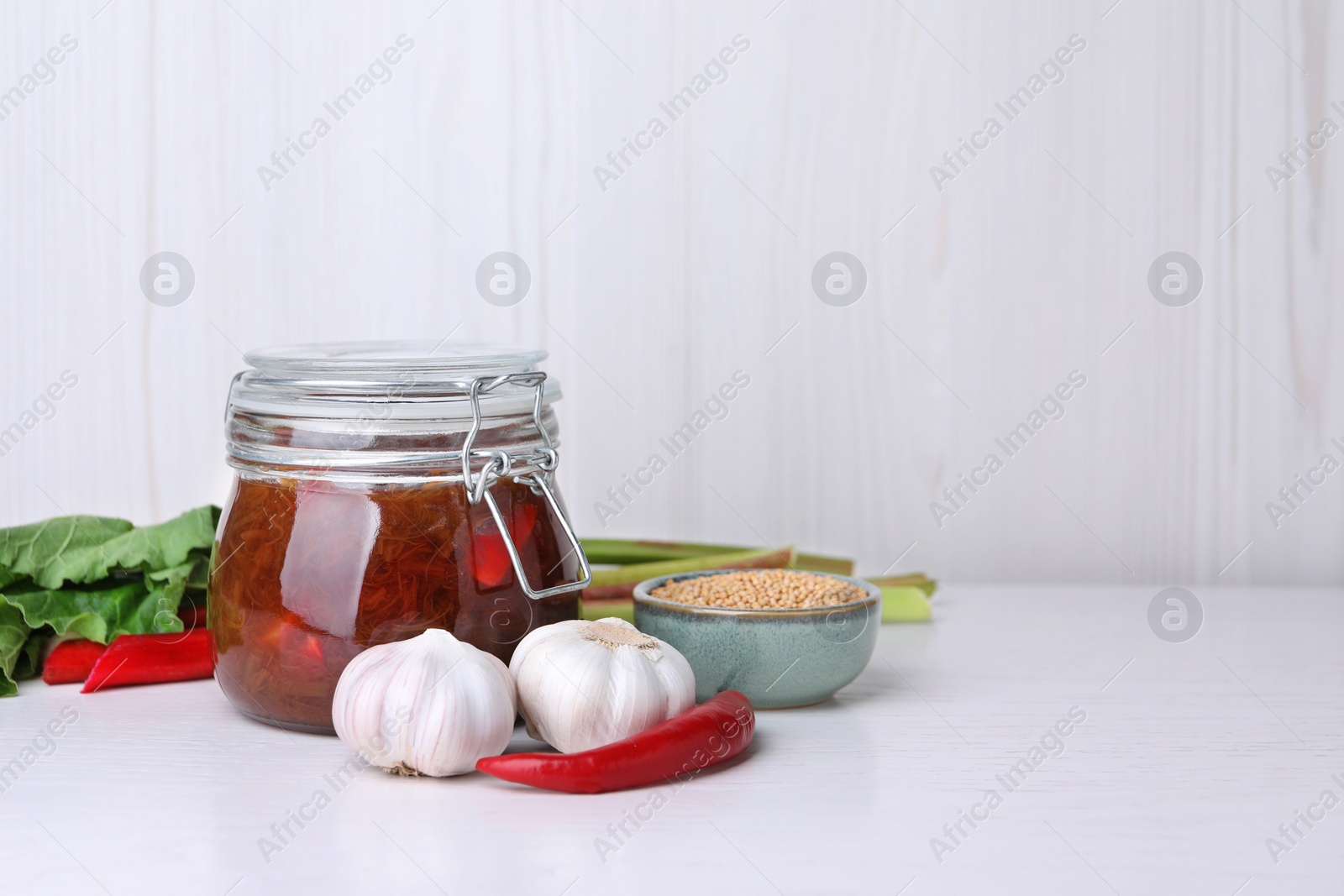 Photo of Tasty rhubarb sauce and ingredients on white table, space for text