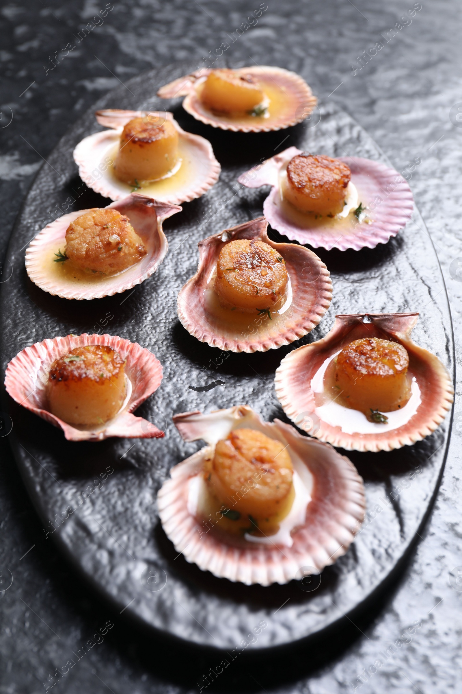 Photo of Delicious fried scallops in shells on black table, closeup