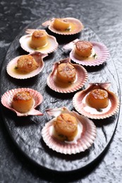 Photo of Delicious fried scallops in shells on black table, closeup