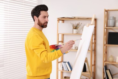 Photo of Man painting in studio. Using easel to hold canvas