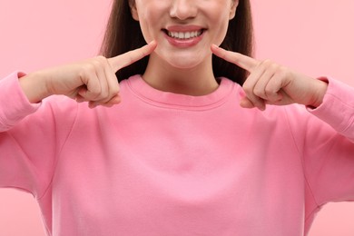 Beautiful woman showing her clean teeth and smiling on pink background, closeup