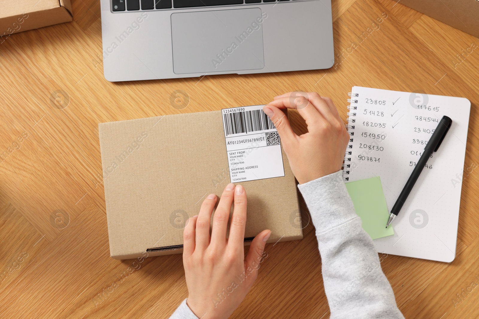 Photo of Woman sticking barcode on parcel at wooden table, top view. Online store