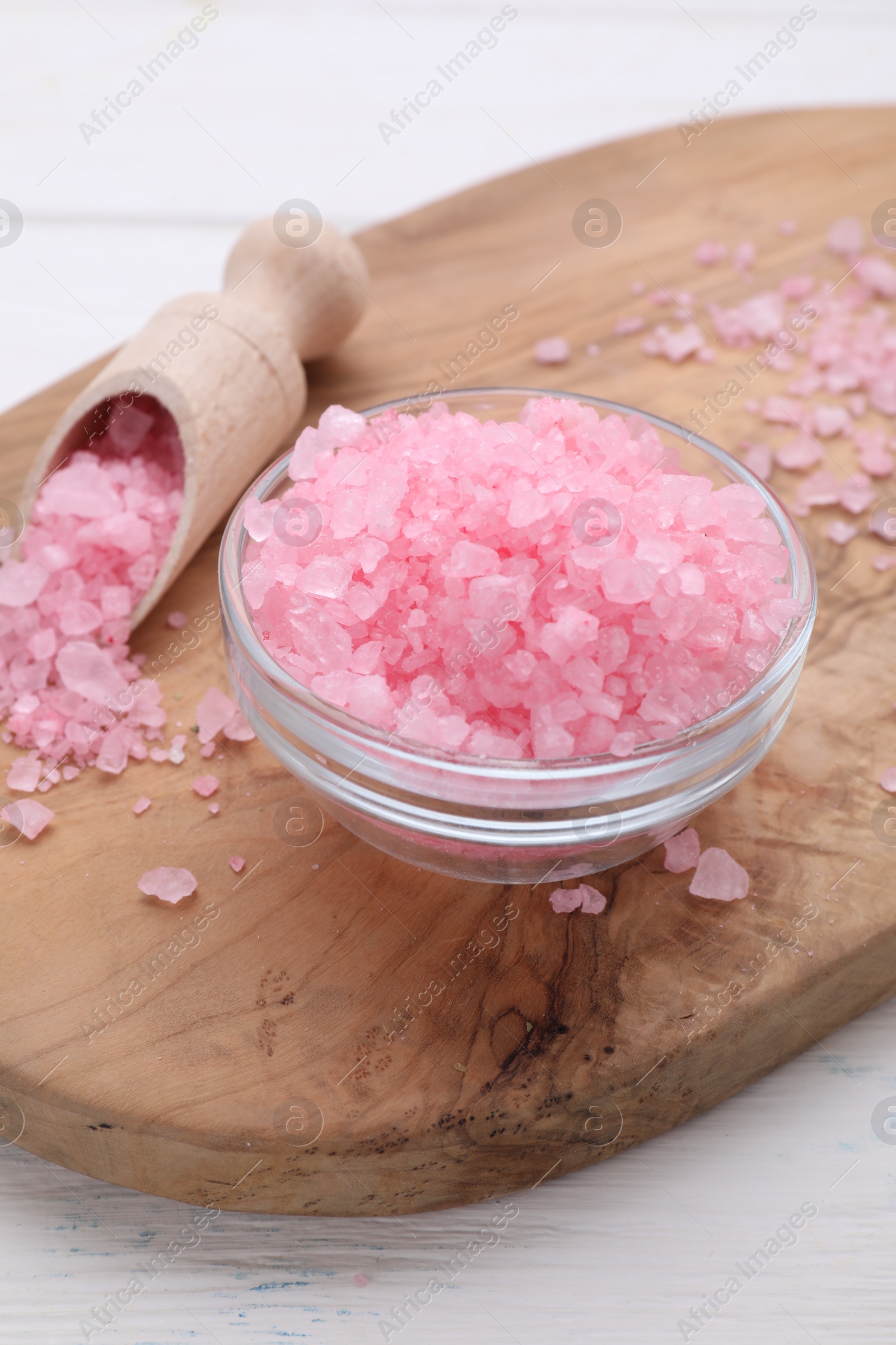 Photo of Bowl and scoop with pink sea salt on white wooden table, closeup