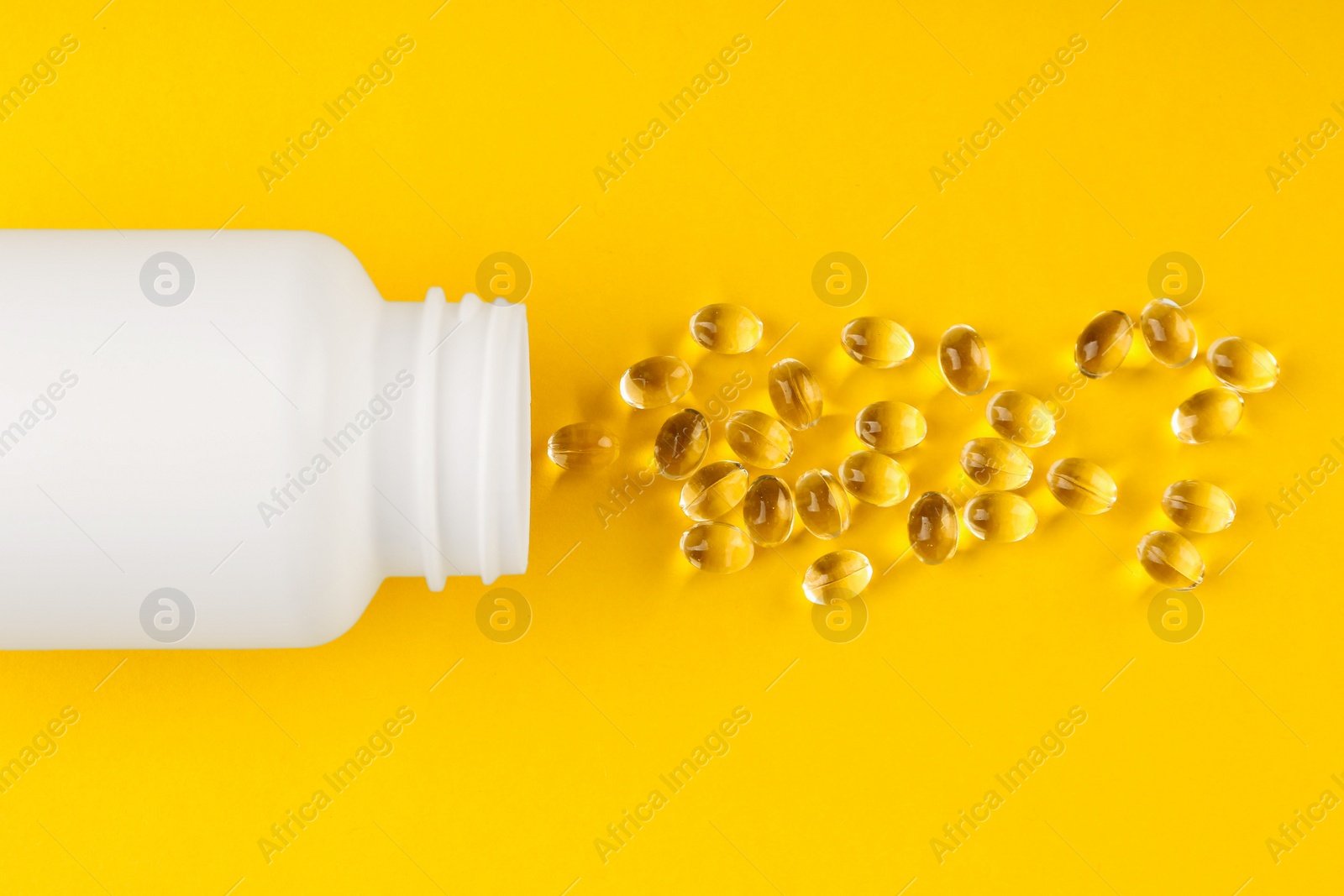 Photo of White medical bottle and vitamin capsules on yellow background, top view