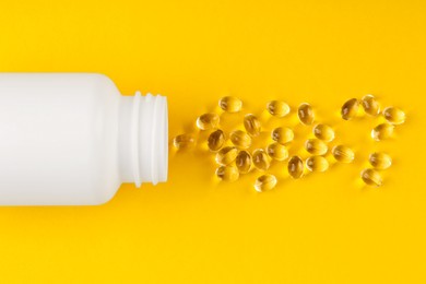 Photo of White medical bottle and vitamin capsules on yellow background, top view