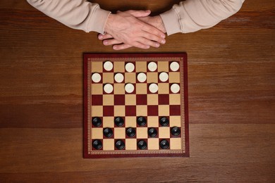 Photo of Playing checkers. Man thinking about next move at wooden table, top view