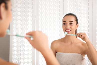 Photo of Woman brushing teeth in front of mirror at home