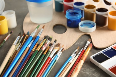 Different brushes, paints and palette on grey table, closeup