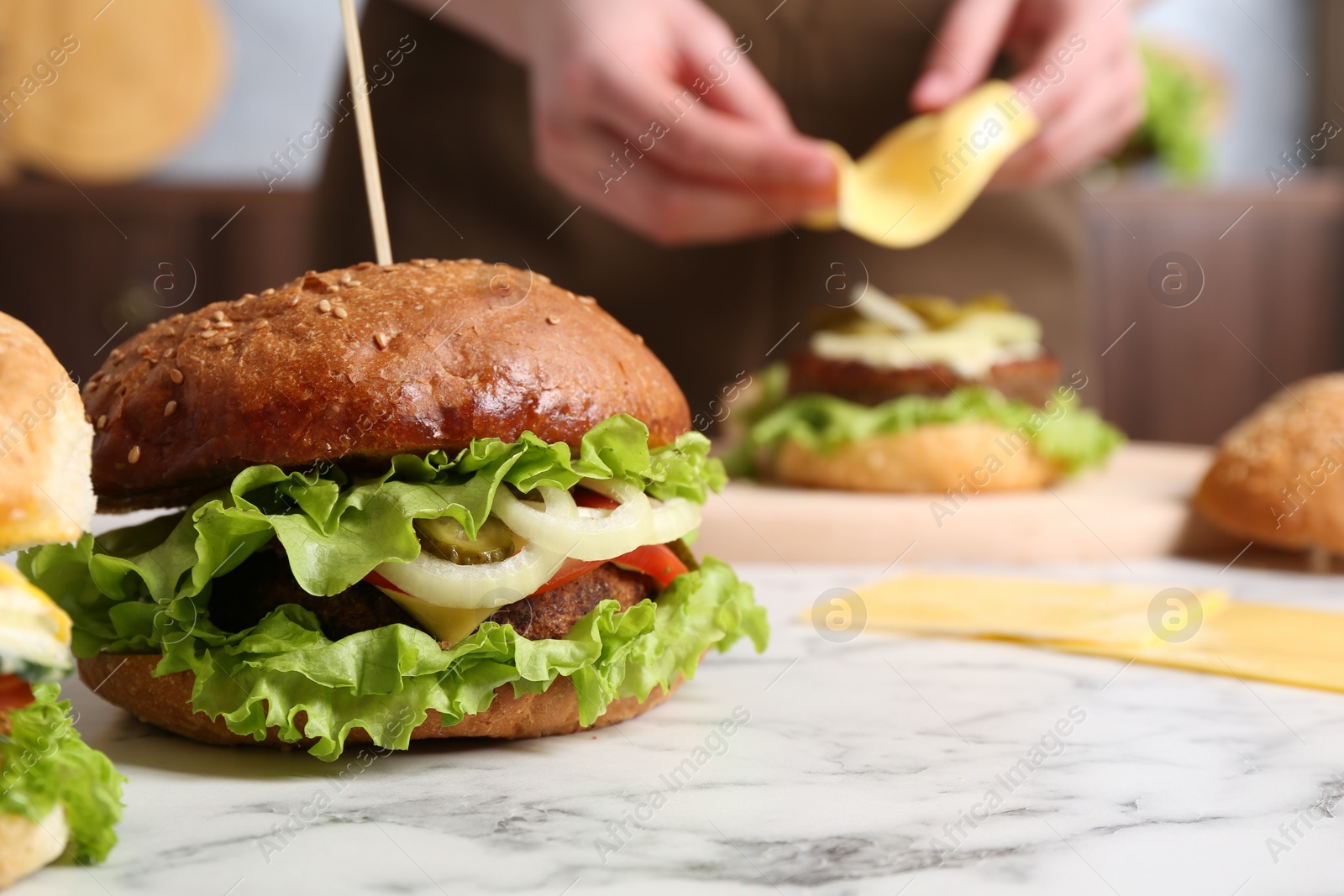 Photo of Woman making delicious vegetarian burger at white marble table, selective focus