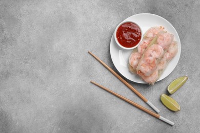 Photo of Tasty spring rolls served with sauce and lime on grey textured table, flat lay. Space for text