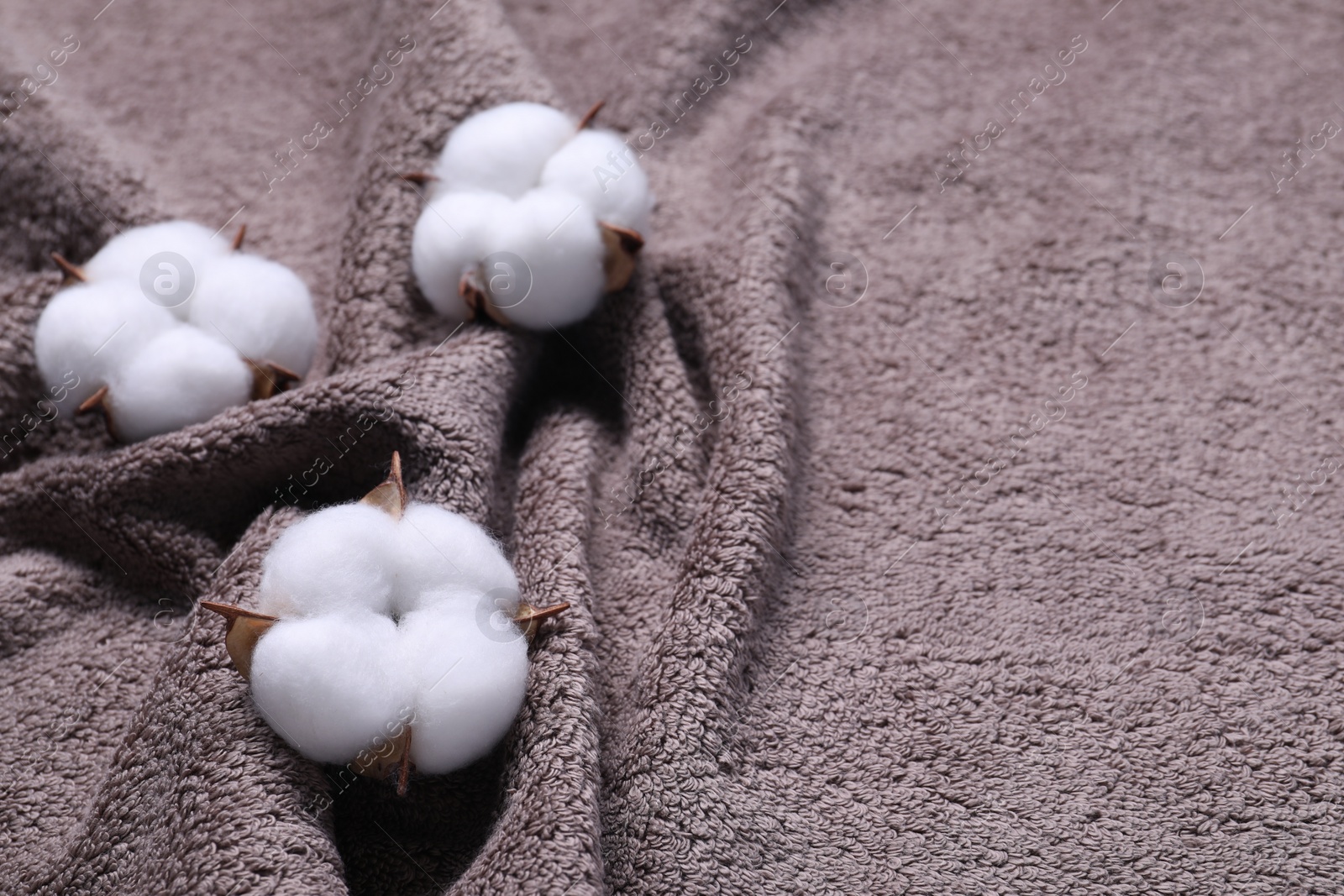 Photo of Fluffy cotton flowers on brown terry towel, closeup. Space for text