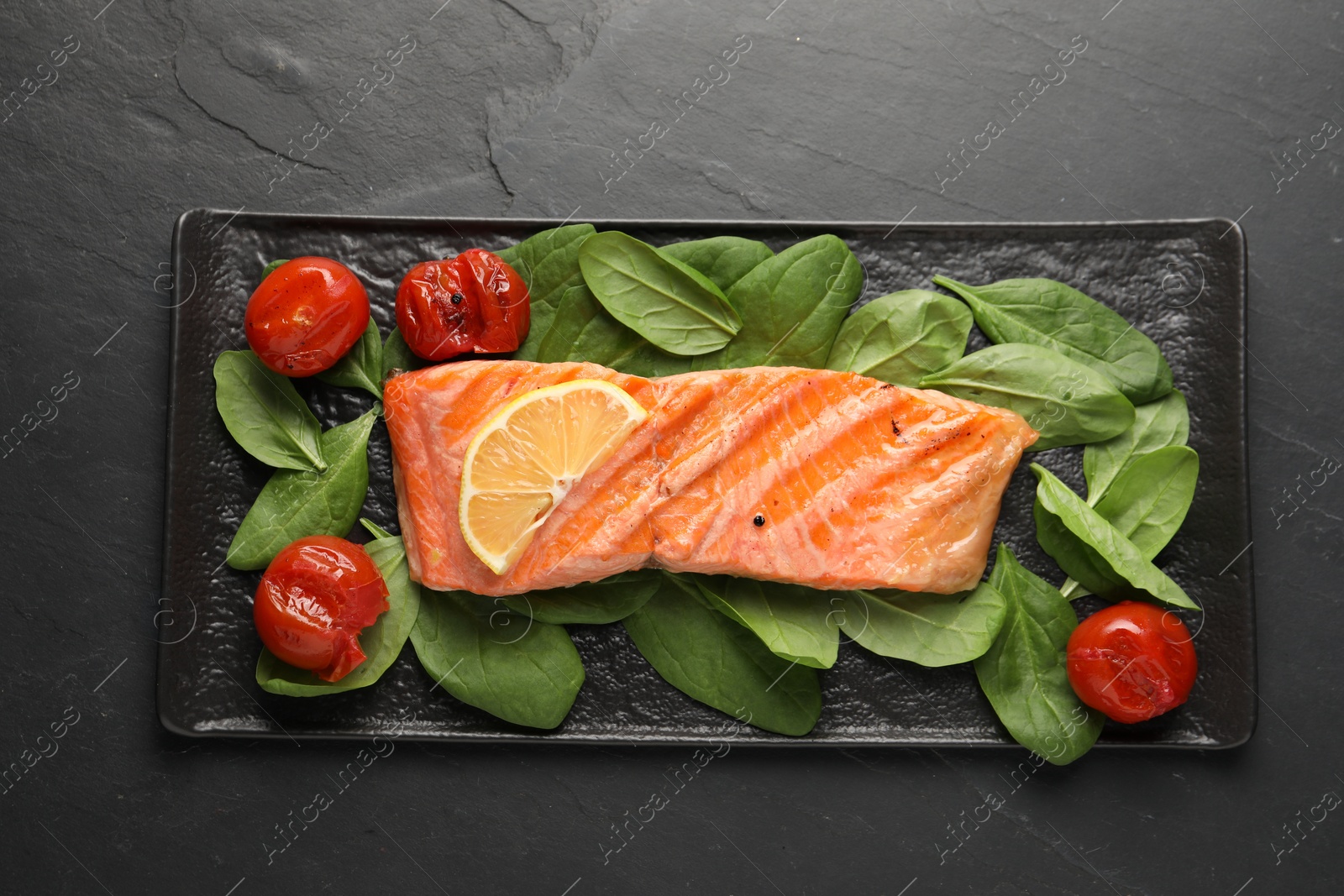 Photo of Tasty grilled salmon with tomatoes and spinach on black table, top view