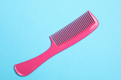 Photo of Modern pink hair comb on light blue background, top view