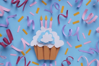 Birthday party. Paper cupcake with candles and confetti on light blue background, flat lay