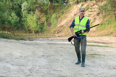 Photo of Man with hunting rifle wearing safety vest outdoors. Space for text