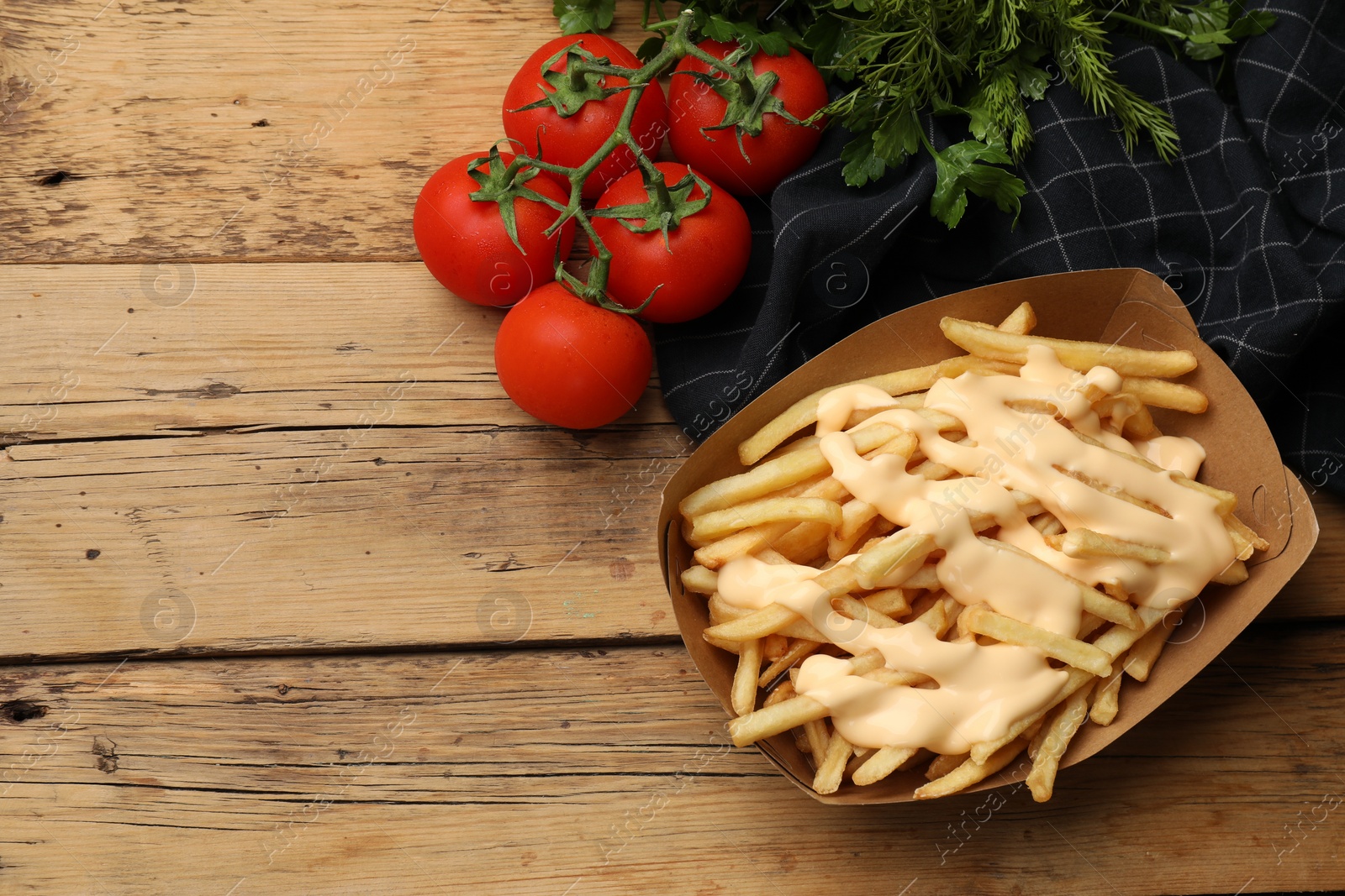 Photo of Delicious French fries with cheese sauce, tomatoes and herbs on wooden table, flat lay. Space for text