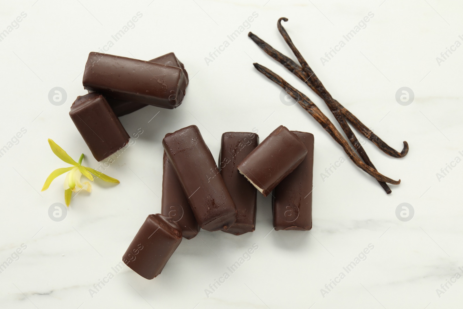 Photo of Glazed curd cheese bars, vanilla pods and flower on white table, flat lay