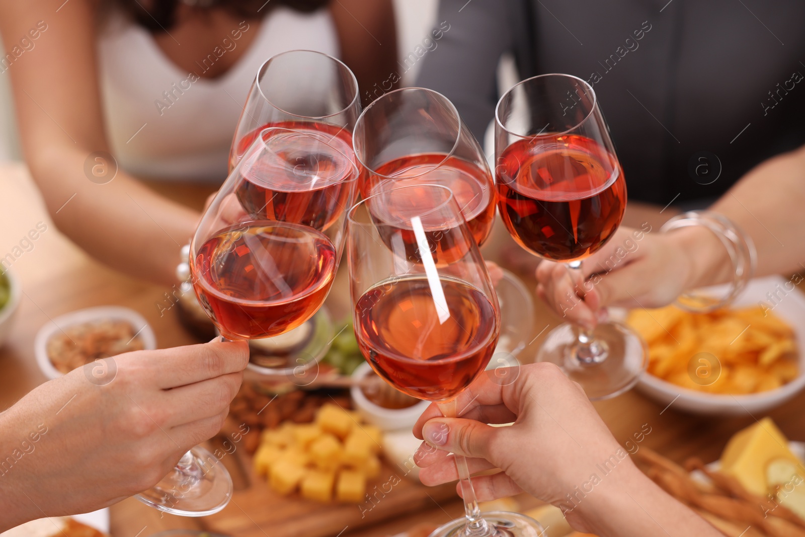 Photo of People clinking glasses with rose wine above wooden table, closeup