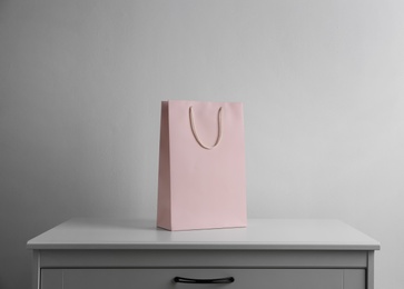 Photo of Paper shopping bag on white chest of drawers against light background