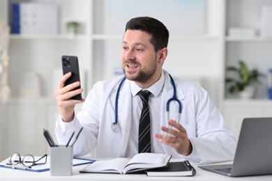 Doctor having online consultation via smartphone at table in clinic