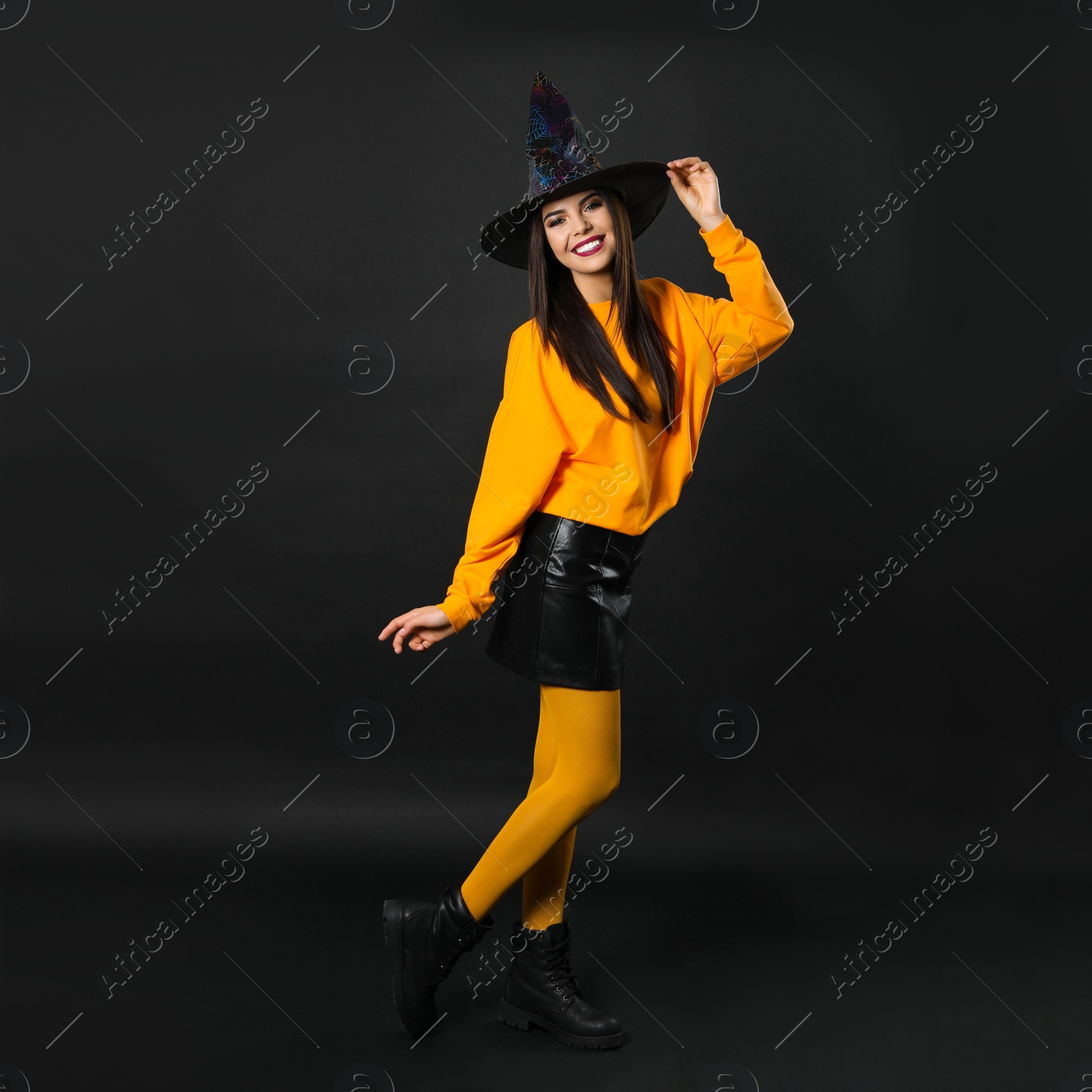 Photo of Beautiful woman wearing witch costume for Halloween party on black background