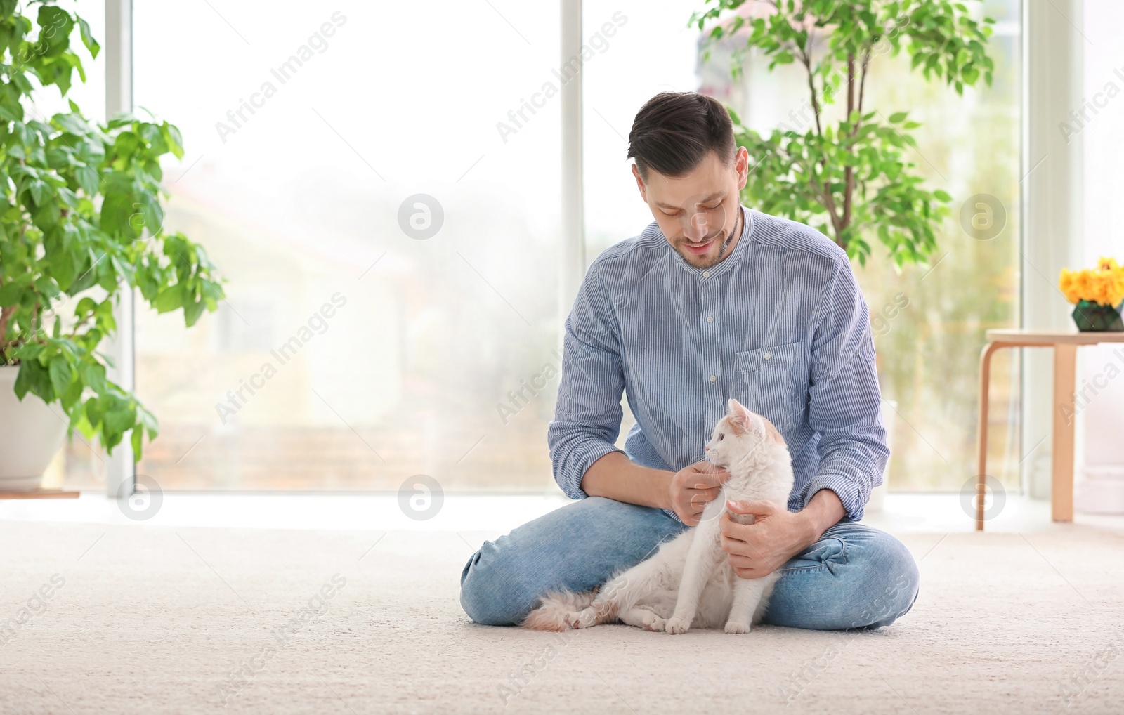 Photo of Young man with cute cat sitting on floor at home