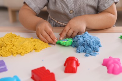 Little girl playing with bright kinetic sand at table indoors, closeup