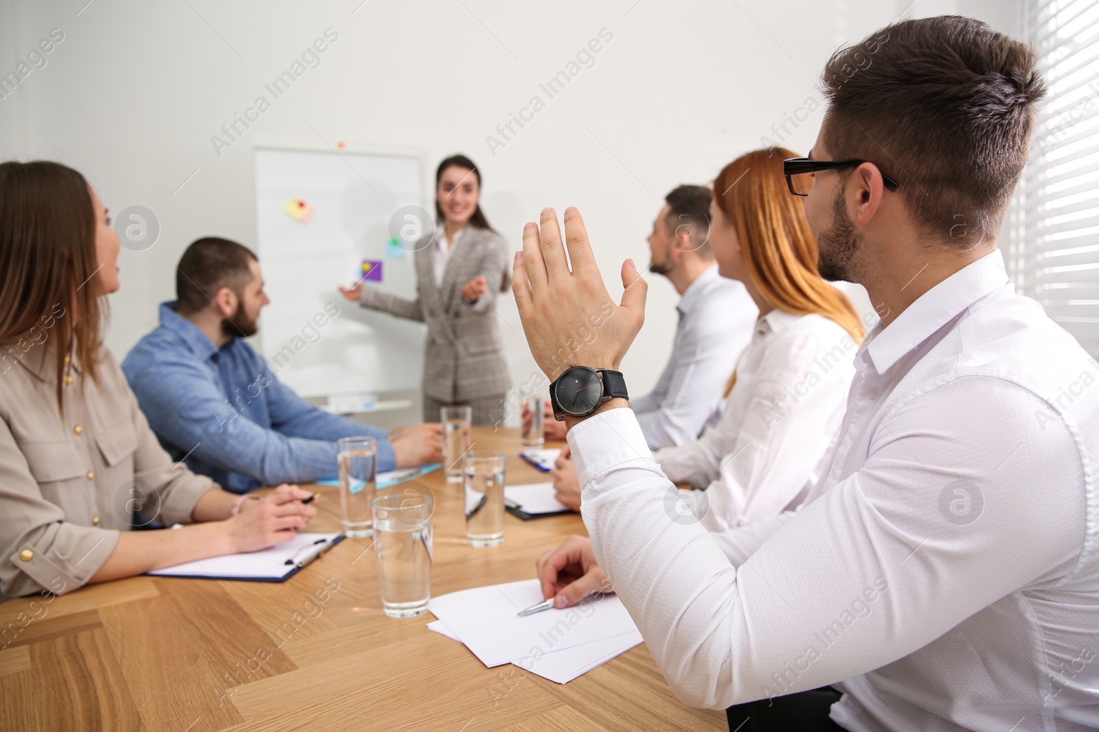 Photo of Young man raising hand to ask question at business training in conference room