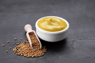 Photo of Bowl of delicious mustard and scoop with seeds on black textured table
