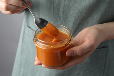 Photo of Woman with delicious persimmon jam on gray background, closeup