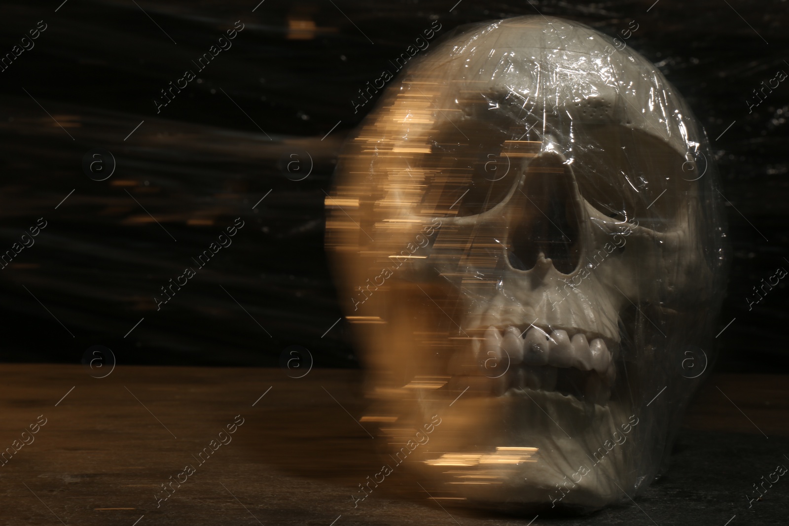 Photo of Human skull with stretch film on stone surface against black background. Space for text