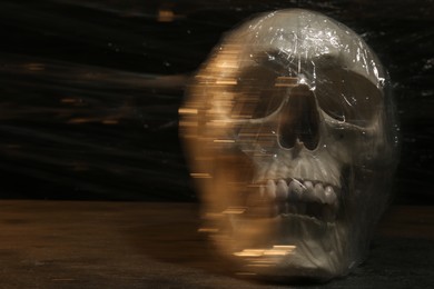 Human skull with stretch film on stone surface against black background. Space for text