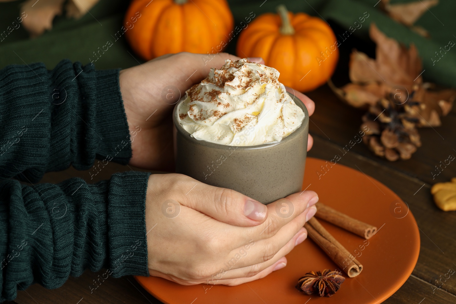 Photo of Woman holding cup of tasty pumpkin spice latte with whipped cream at wooden table, closeup