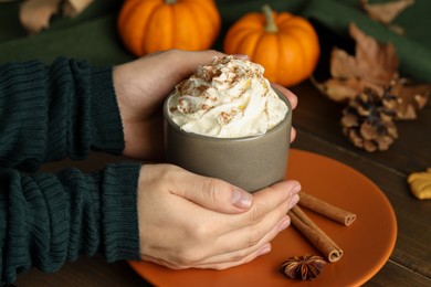 Photo of Woman holding cup of tasty pumpkin spice latte with whipped cream at wooden table, closeup