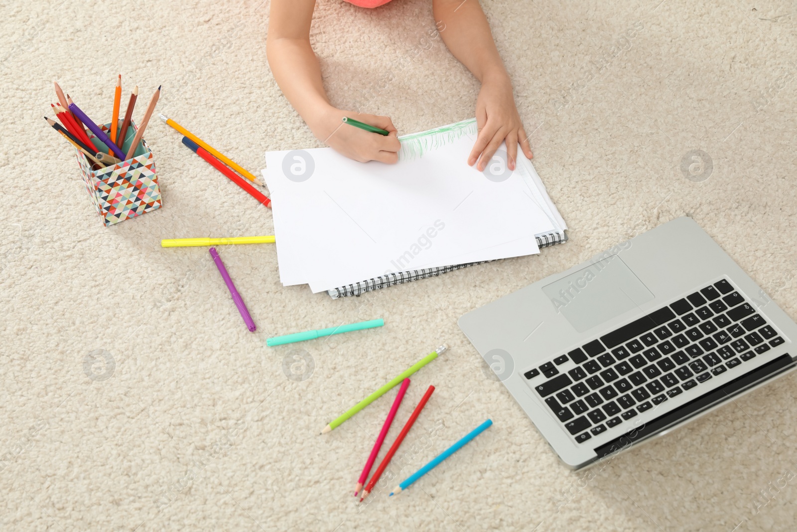 Photo of Little girl drawing on paper with pencil at online lesson indoors, closeup. Distance learning