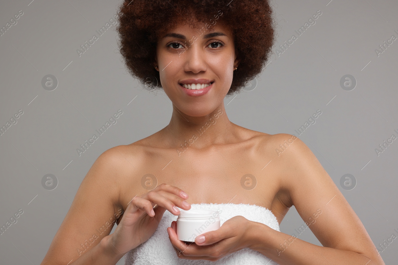 Photo of Beautiful young woman holding body cream on grey background