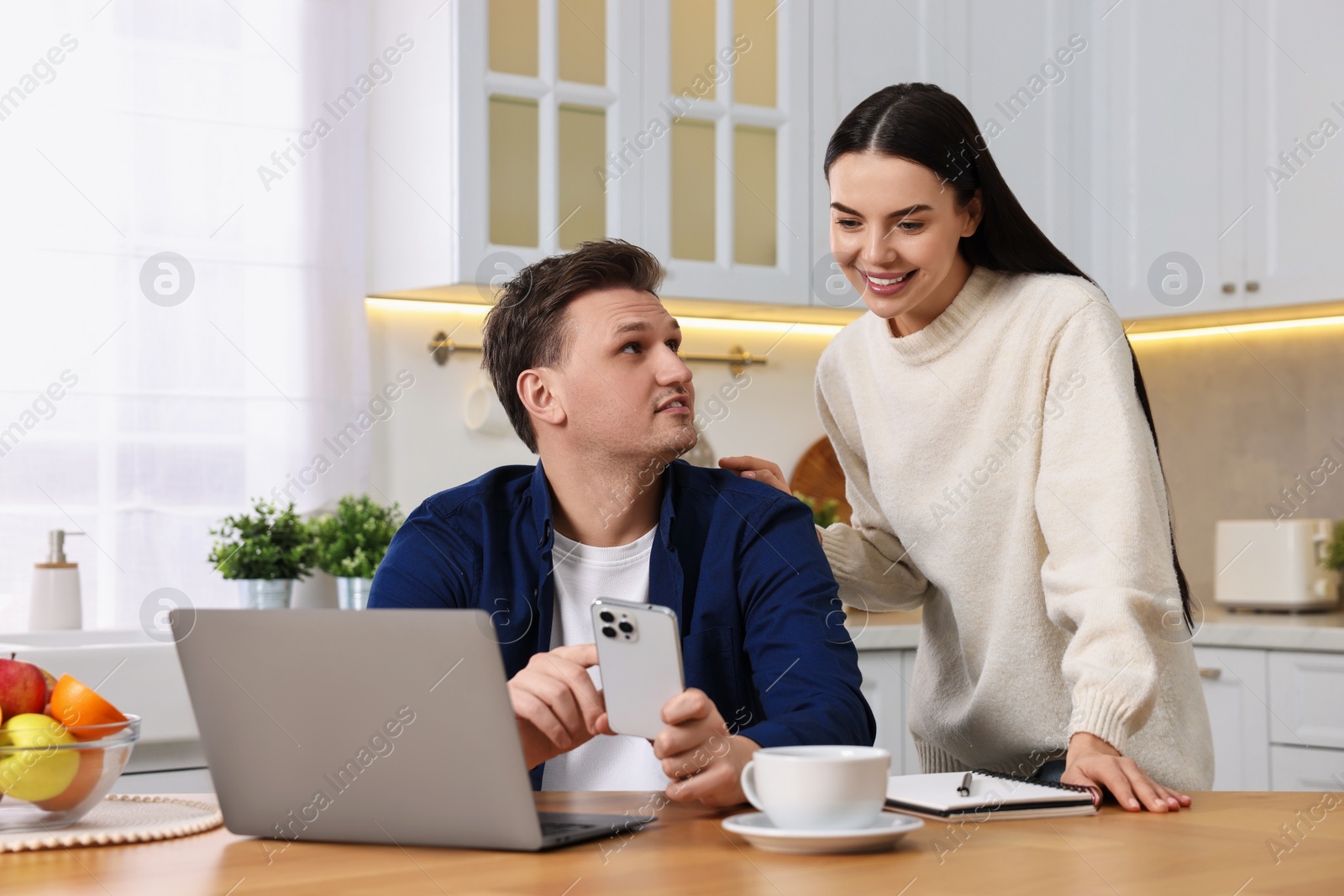 Photo of Happy couple using smartphone together at wooden table in kitchen