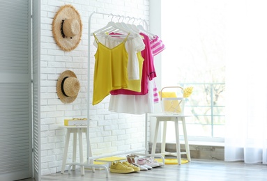 Photo of Wardrobe rack with women's clothes and different shoes at white brick wall in room