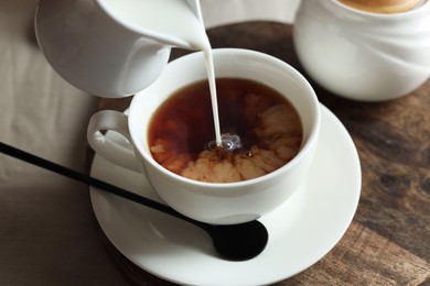 Photo of Pouring milk into cup with tea on light table, closeup